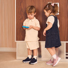 Two children standing in front of a wooden door, one holding a blue toy.